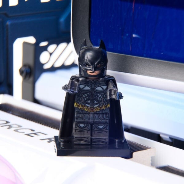 Karanlık kostümlü Batman LEGO figürü, bilgisayar ekranı önünde duruyor, masa üzerinde, detaylı tasarımıyla dikkat çekiyor.