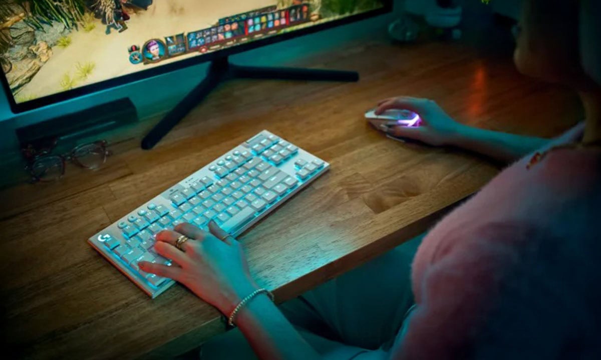 Yapay zeka destekli gaming monitörü ve mouse ile masa başında oyun oynayan genç kadın, bilgisayar oyunları ve e-spor hazırlıkları yaparken, RGB aydınlatmalı klavye ve yüksek çözünürlüklü oyun ekranı ile oyun deneyimini en üst seviyeye çıkarıyor.